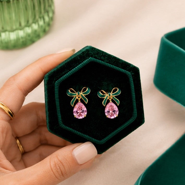 Green velvet jewelry box with pink teardrop earrings held by a hand.