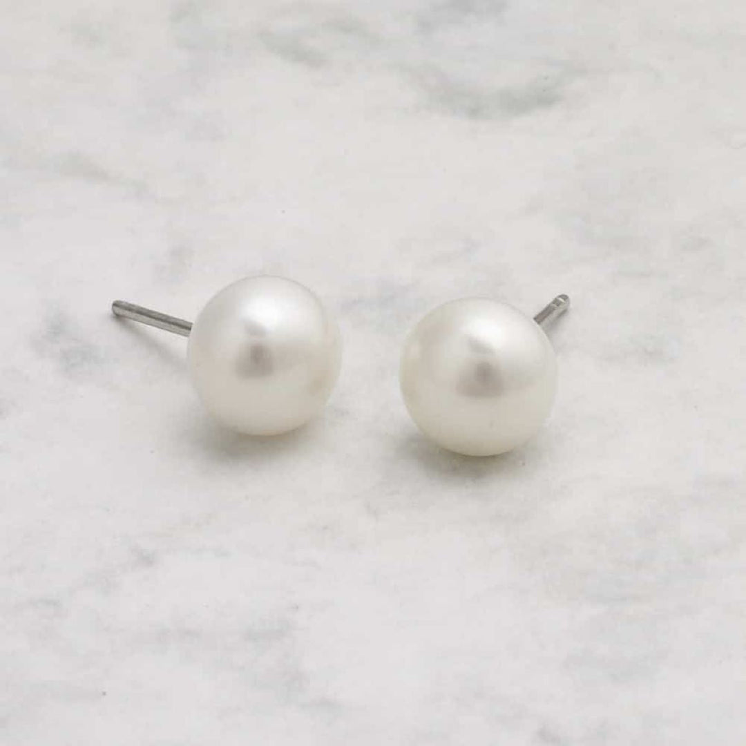 Niche Jewellery 9mm white freshwater pearl stud earrings set in sterling silver on a marble surface