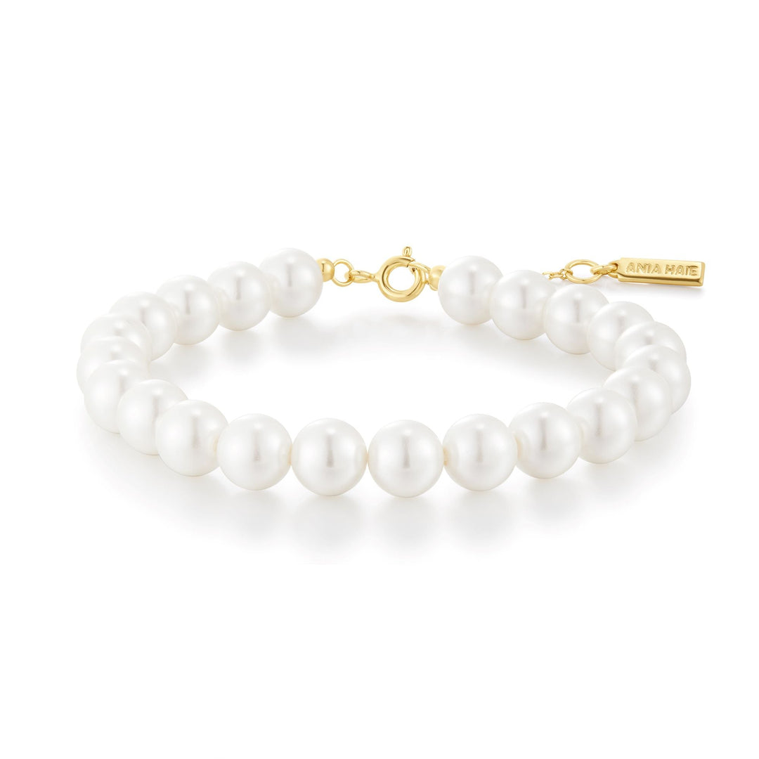 Niche Jewellery Ania Haie shell pearl beaded bracelet with gold-toned clasp and branded charm on white background
