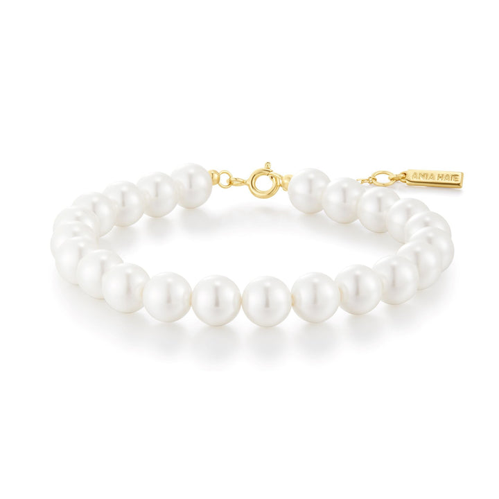 Niche Jewellery Ania Haie shell pearl beaded bracelet with gold-toned clasp and branded charm on white background