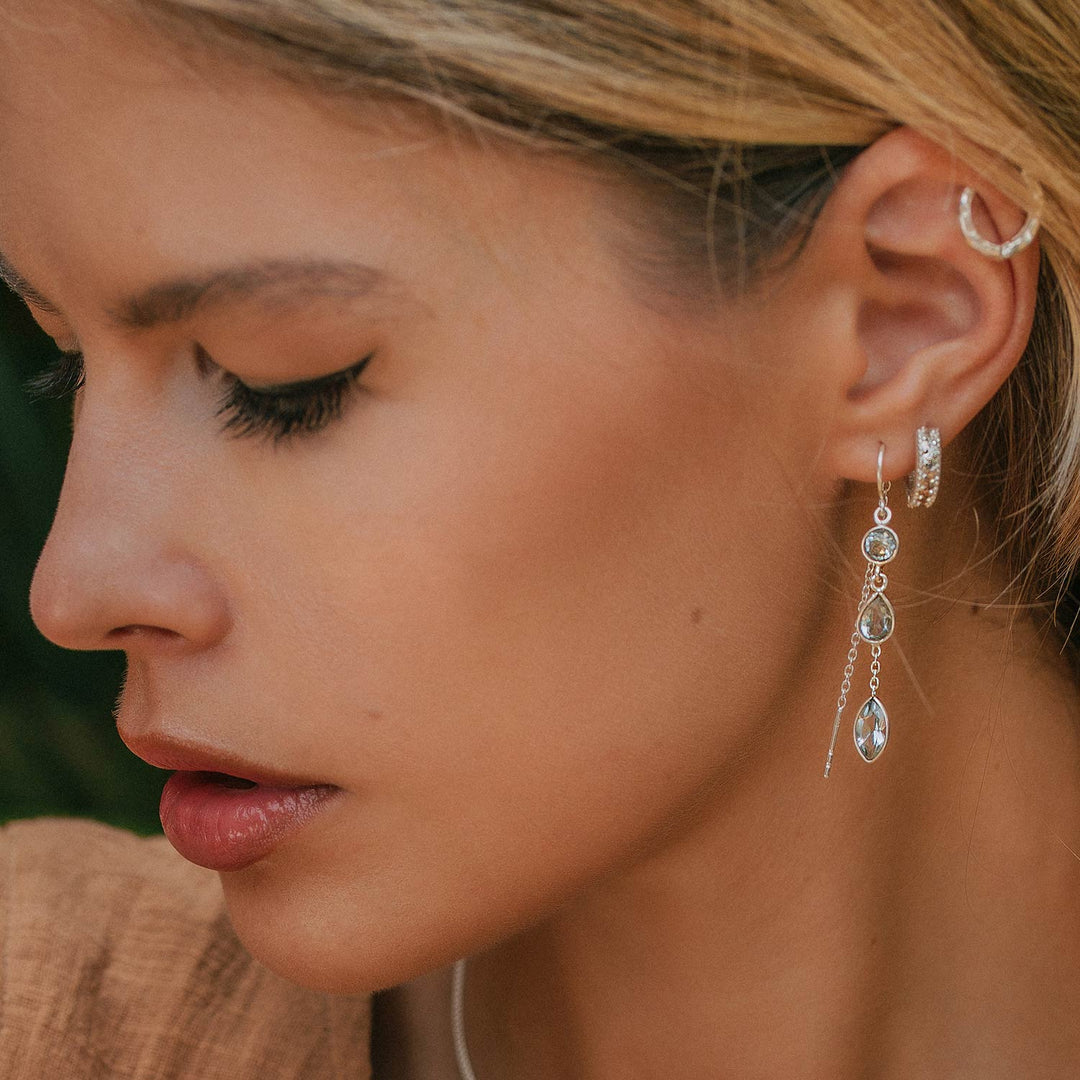 Niche Jewellery Charlotte's Web Azura sterling silver threader earrings with blue topaz stones worn by a woman.