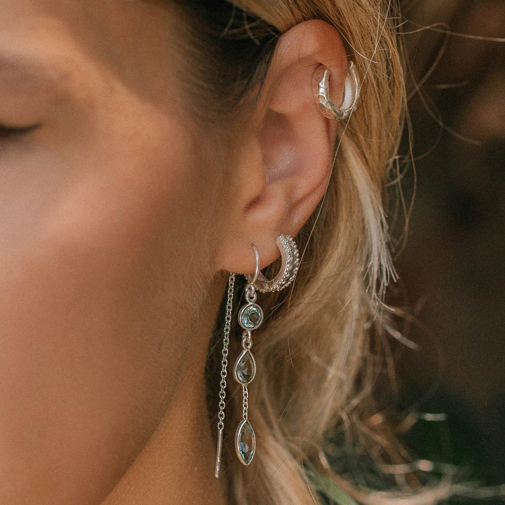 Niche Jewellery Charlotte's Web Azura sterling silver threader earrings with blue topaz stones worn on a model's ear.