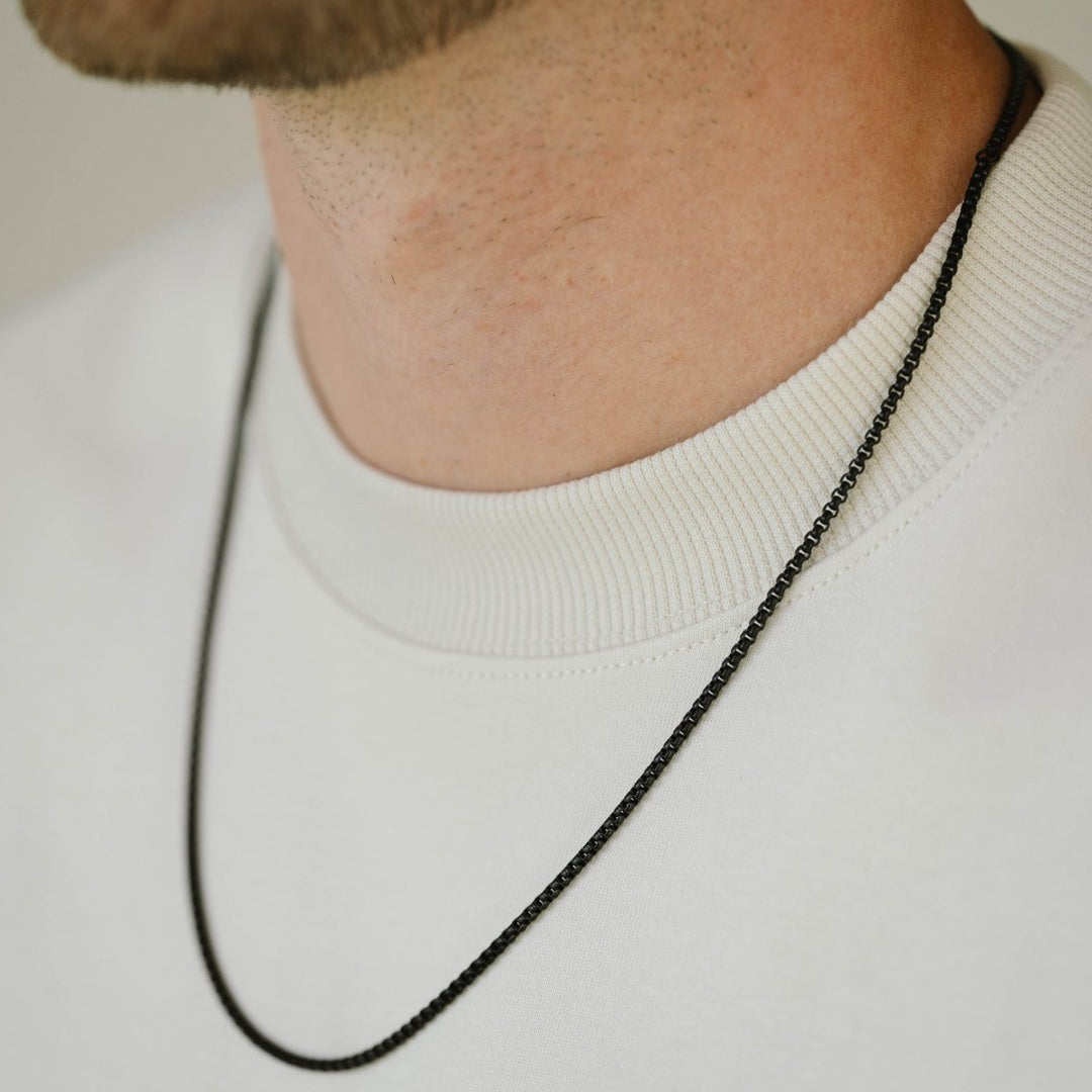 Niche Jewellery thin black box chain necklace in stainless steel worn by a man in a white crew neck shirt