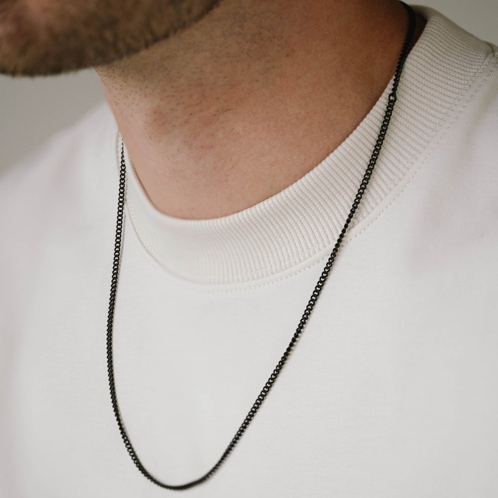Niche Jewellery Steel & Barnett thin black stainless steel curb chain necklace worn by a man in a white sweater.