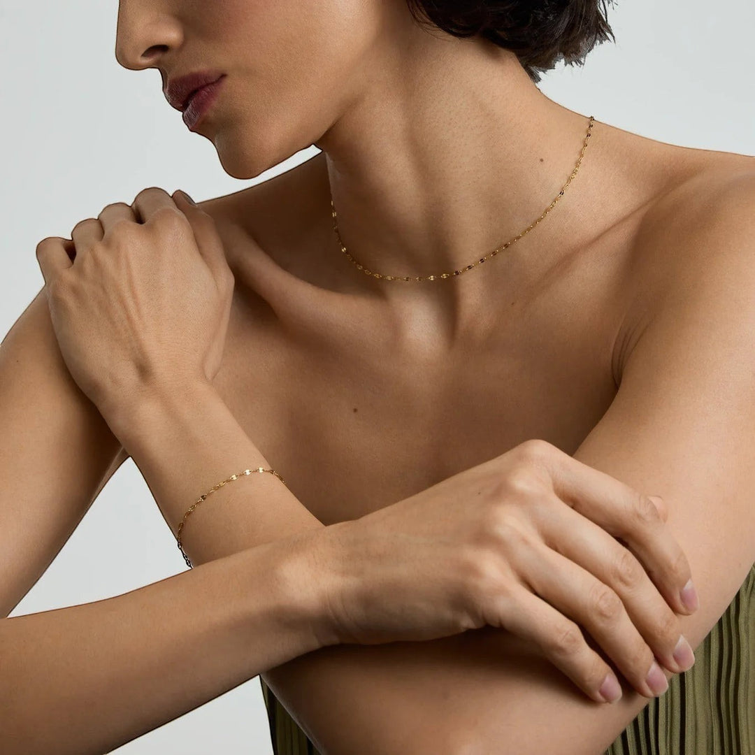 Niche Jewellery D.Louise dainty gold chain necklace and matching bracelet worn by a woman for a minimalist layered look.
