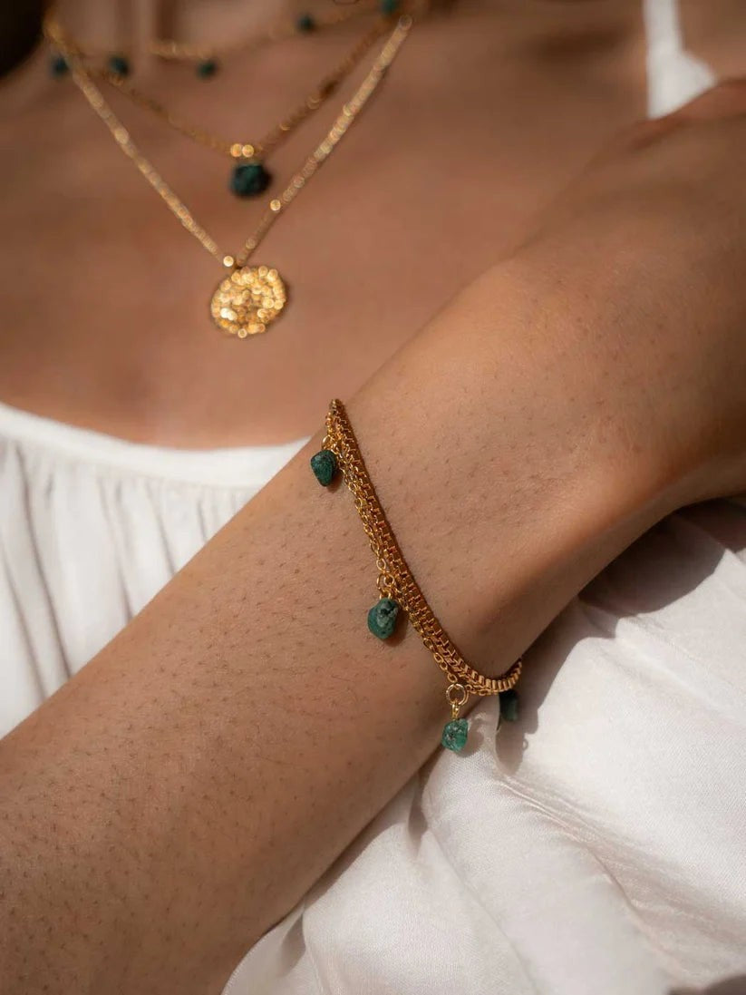 Niche Jewellery gold plated chain bracelet featuring raw-cut emerald charms worn on a woman's wrist