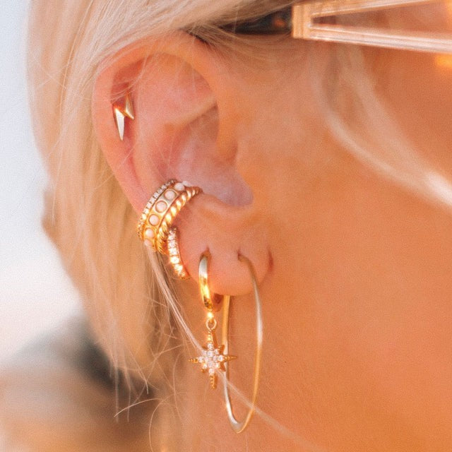 Niche Jewellery Scream Pretty flat gold hoop earrings worn in a layered ear stack with other gold jewellery pieces.