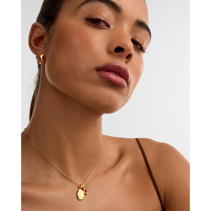 Niche Jewellery Katie Loxton gold necklace with a red January birthstone pendant worn by a model.