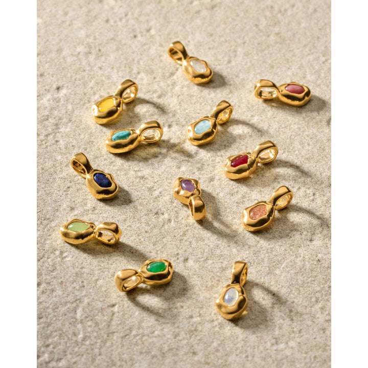 Niche Jewellery Katie Loxton waterproof gold birthstone pendants in various colors on a textured stone surface
