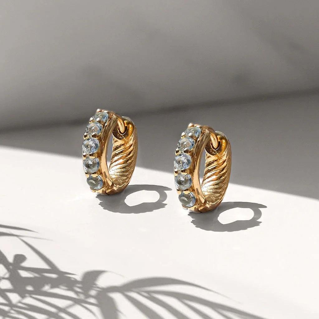 Niche Jewellery Charlotte's Web Kali huggie hoops in 24ct gold plated brass with faceted blue topaz stones.