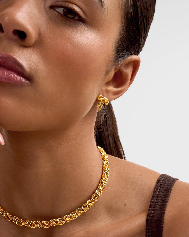Niche Jewellery Katie Loxton Novelle waterproof gold bow stud earrings worn on a model with a matching gold necklace