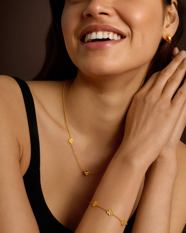 Niche Jewellery Katie Loxton gold-tone waterproof charm bracelet worn on a model's wrist with matching necklace
