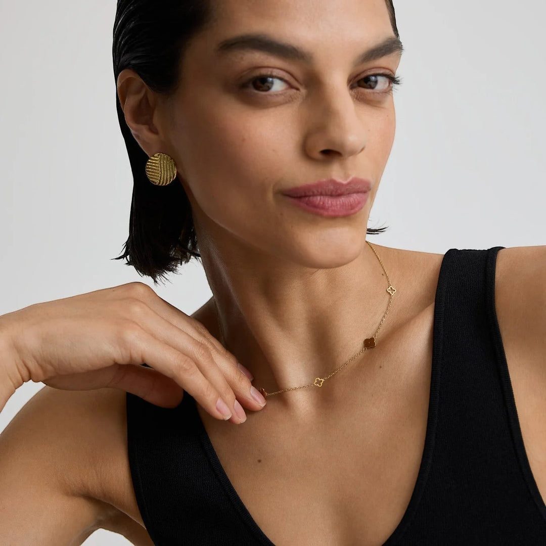 Niche Jewellery D.Louise gold clover necklace with cut-out and solid charms on a model wearing a black tank top.