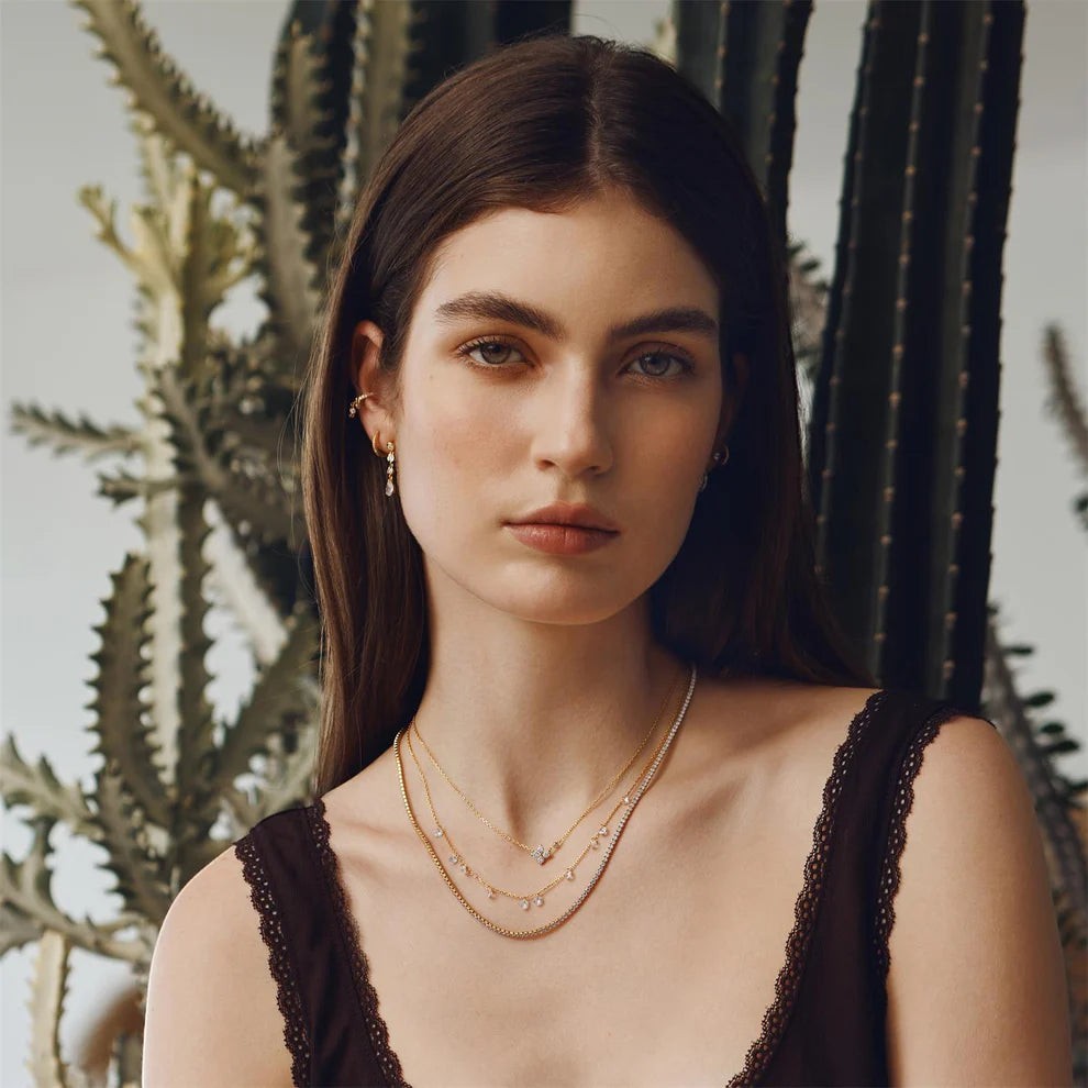 Model wearing Niche Jewellery Ania Haie gold clover necklace with cubic zirconia layered with delicate gold chains.