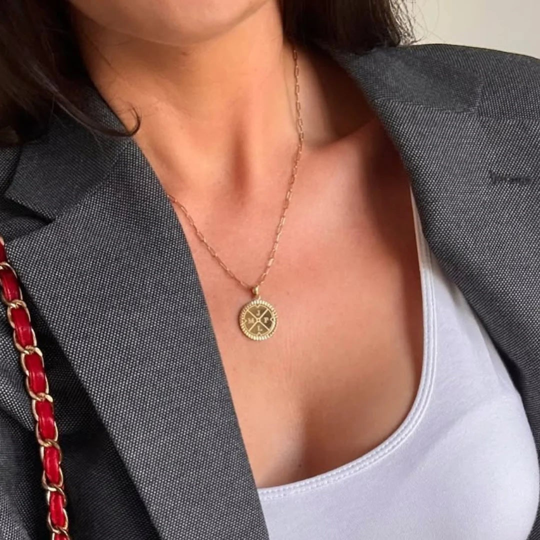 Niche Jewellery D.Louise gold compass pendant necklace with engraved initials worn on a delicate chain over a white top.