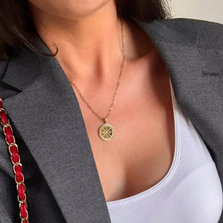 Niche Jewellery D.Louise gold compass pendant necklace with engraved initials worn on a delicate chain over a white top.