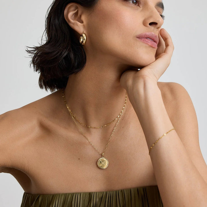 Niche Jewellery D.Louise gold compass pendant necklace worn by a woman with matching gold hoop earrings