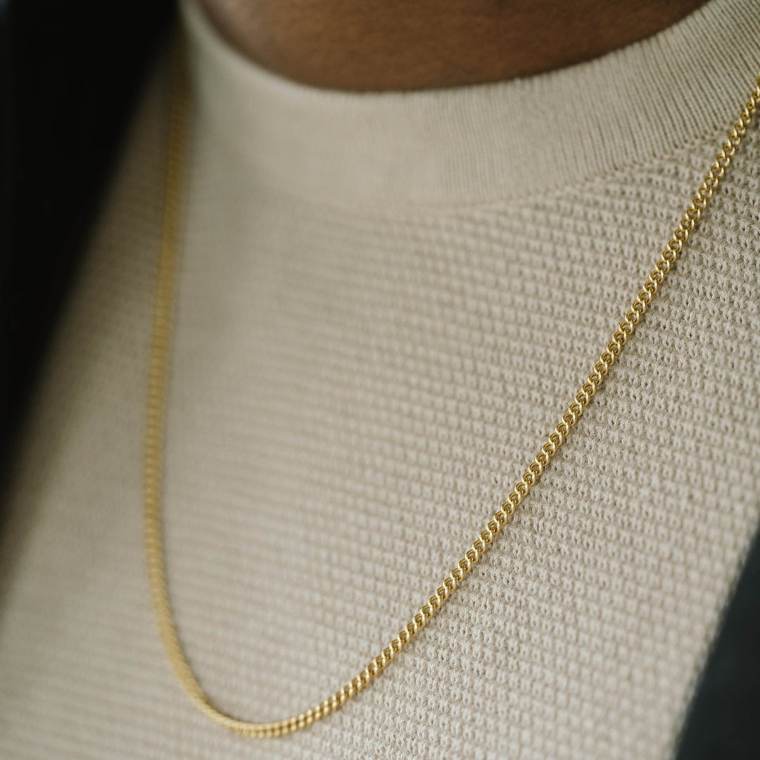 Niche Jewellery thin 18K gold plated stainless steel curb chain necklace worn on a man in a cream sweater