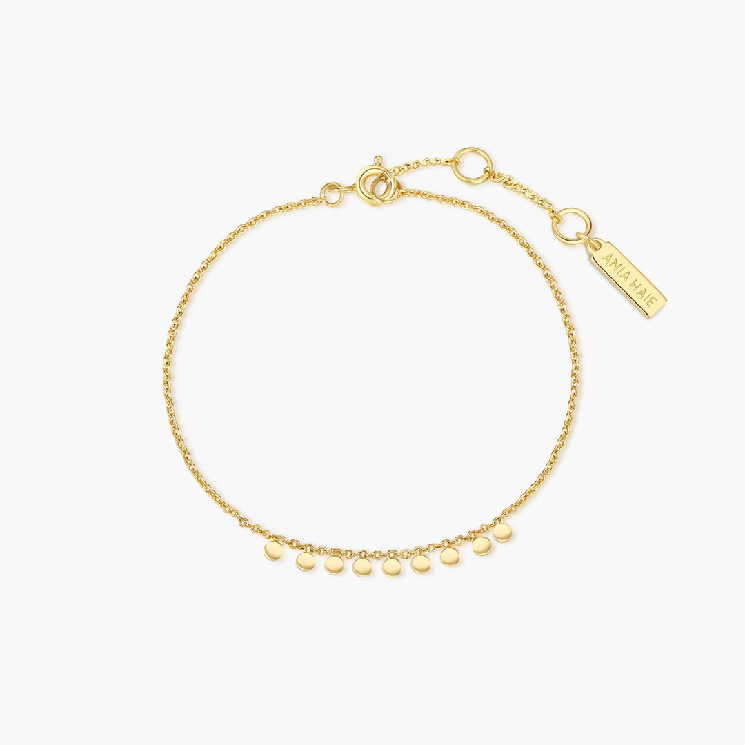 Niche Jewellery Ania Haie gold chain bracelet featuring small dangling discs and a branded rectangular charm.