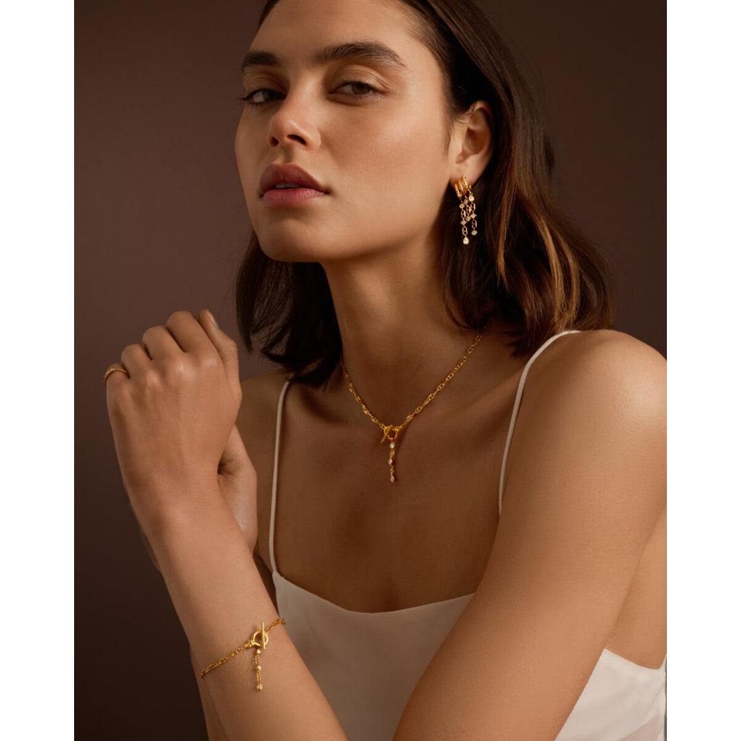 Niche Jewellery Katie Loxton gold drop earrings worn by a model with a matching necklace and bracelet