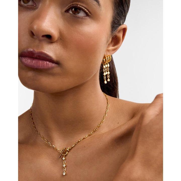 Niche Jewellery Katie Loxton gold drop earrings with sparkling accents worn by a model with a matching gold necklace.