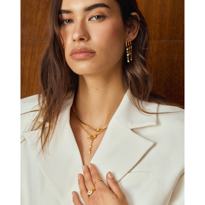 Niche Jewellery Katie Loxton waterproof gold drop earrings worn by a woman in a white blazer
