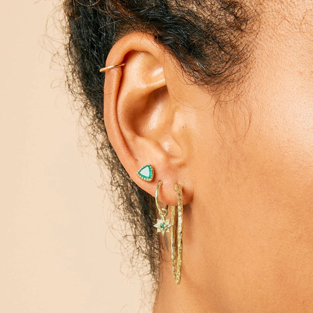 Niche Jewellery Charlotte's Web gold hammered hoop earrings worn on a model's ear with other delicate studs.