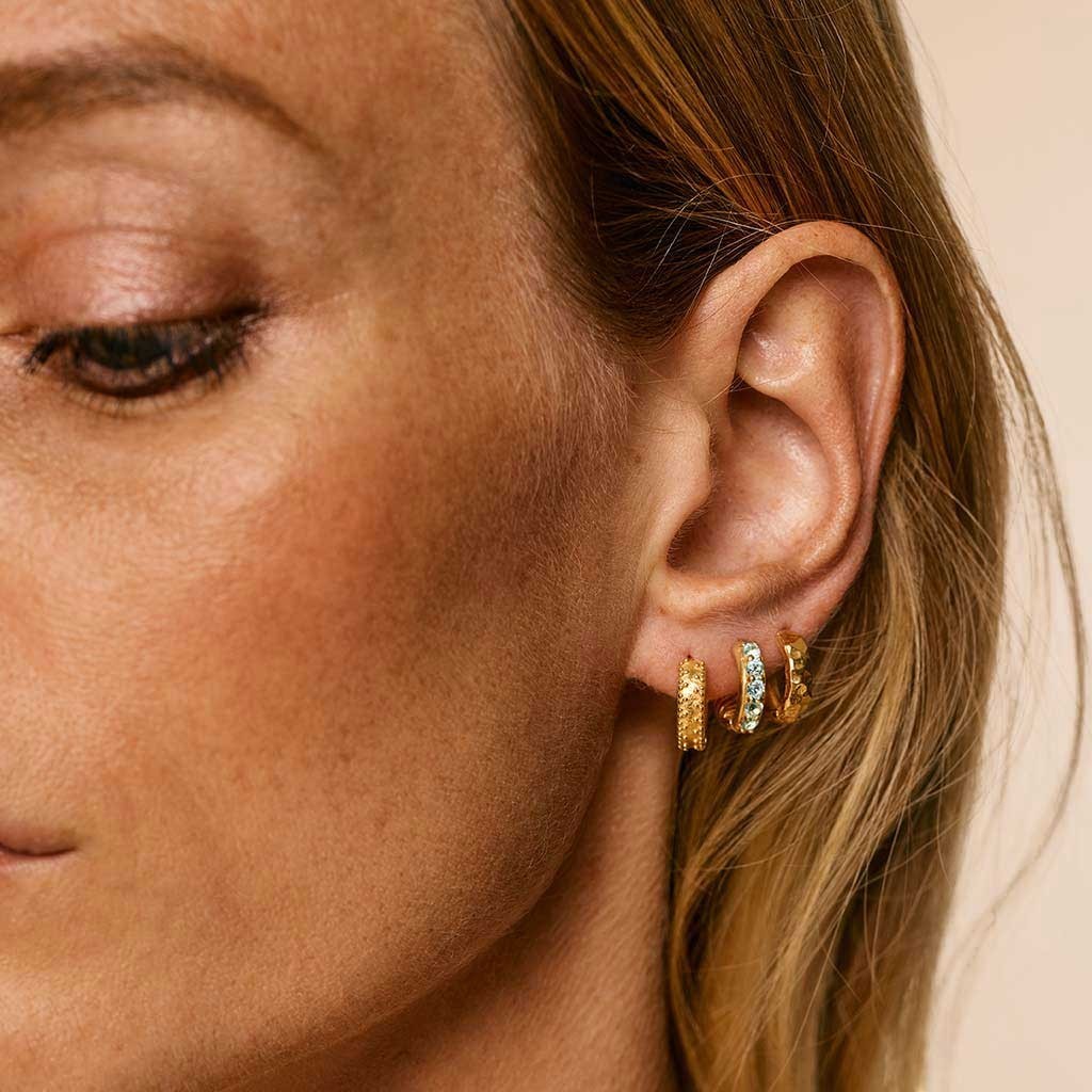 Niche Jewellery Charlotte's Web gold vermeil hammered huggie hoops worn on a model's earlobe.