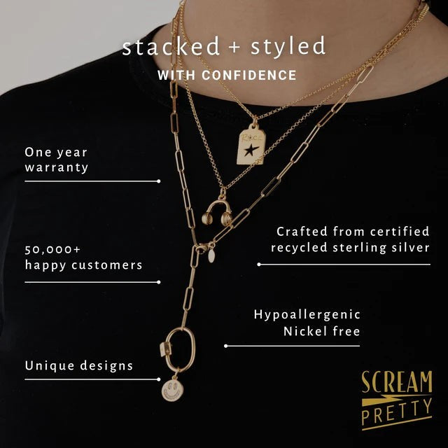 Niche Jewellery Scream Pretty gold headphones pendant necklace layered with other gold chains on a person wearing a black top.