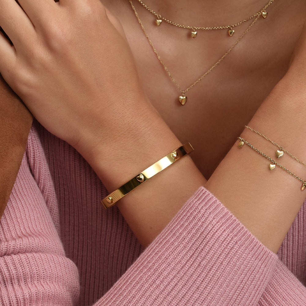 Niche Jewellery Olivia Burton gold-plated bangle featuring mini heart charms worn on a wrist with matching jewelry