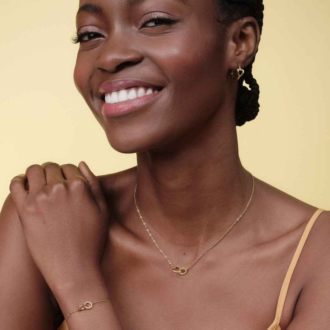 Niche Jewellery Olivia Burton gold-plated hoop earrings with interlinking heart design worn by a smiling woman