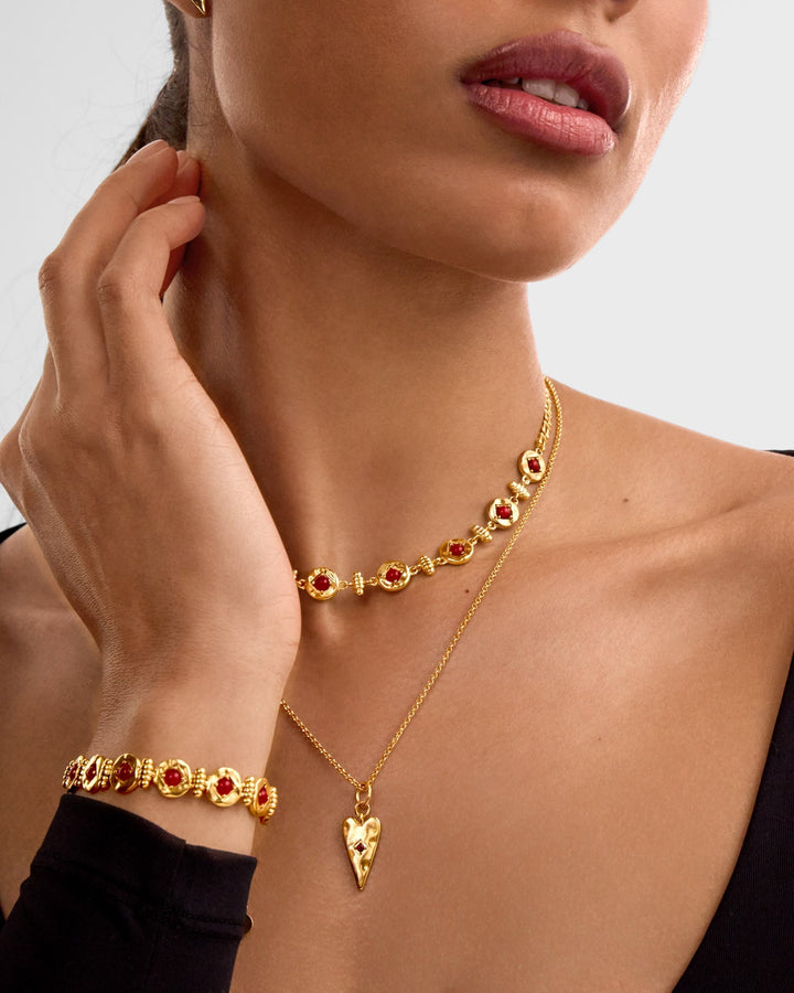 Niche Jewellery Katie Loxton gold heart necklace with red stone detail worn layered on a model