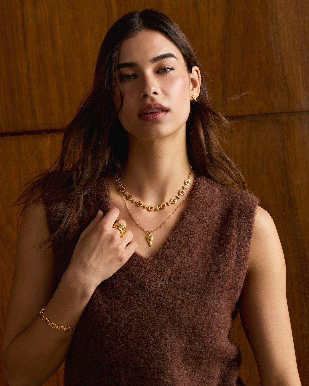 Niche Jewellery Katie Loxton gold heart necklace with red accents worn by a model in a brown knit vest