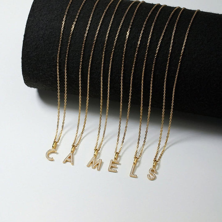 Niche Jewellery Ania Haie gold initial letter necklaces with pavé crystals on delicate chains displayed on a black stand.