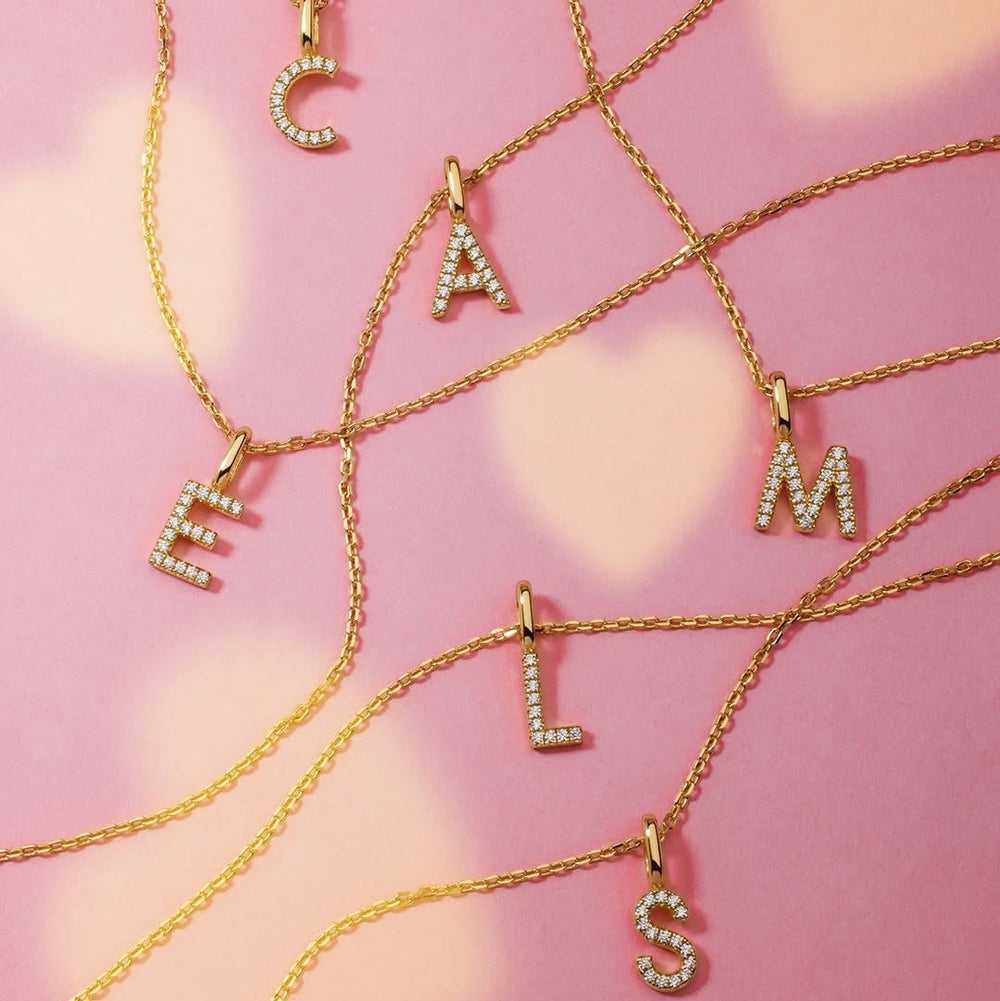 Niche Jewellery Ania Haie gold initial necklaces with sparkling pavé stones arranged on a soft pink background