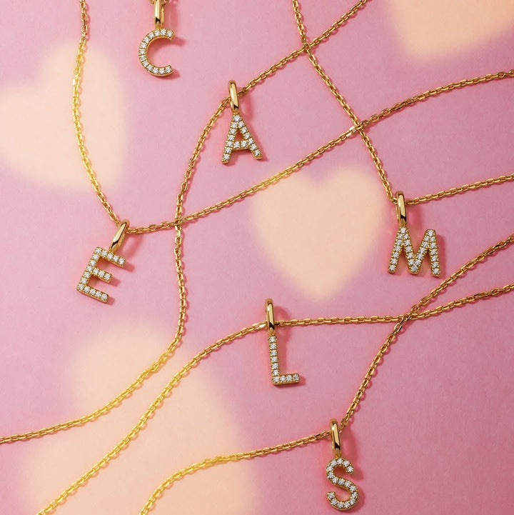 Niche Jewellery Ania Haie gold initial necklaces with sparkling pavé stones arranged on a soft pink background