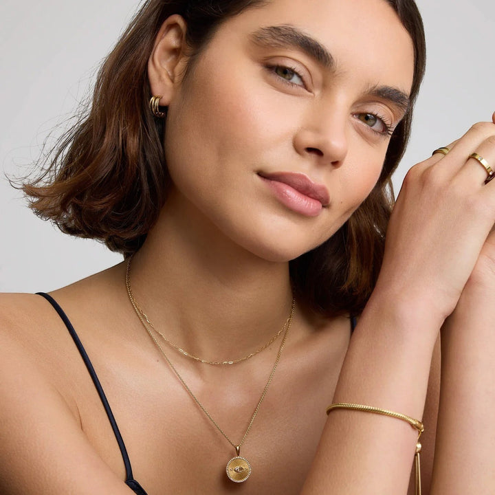 Niche Jewellery D.Louise gold intertwined mini hoop earrings worn by a woman with a layered necklace and bracelet