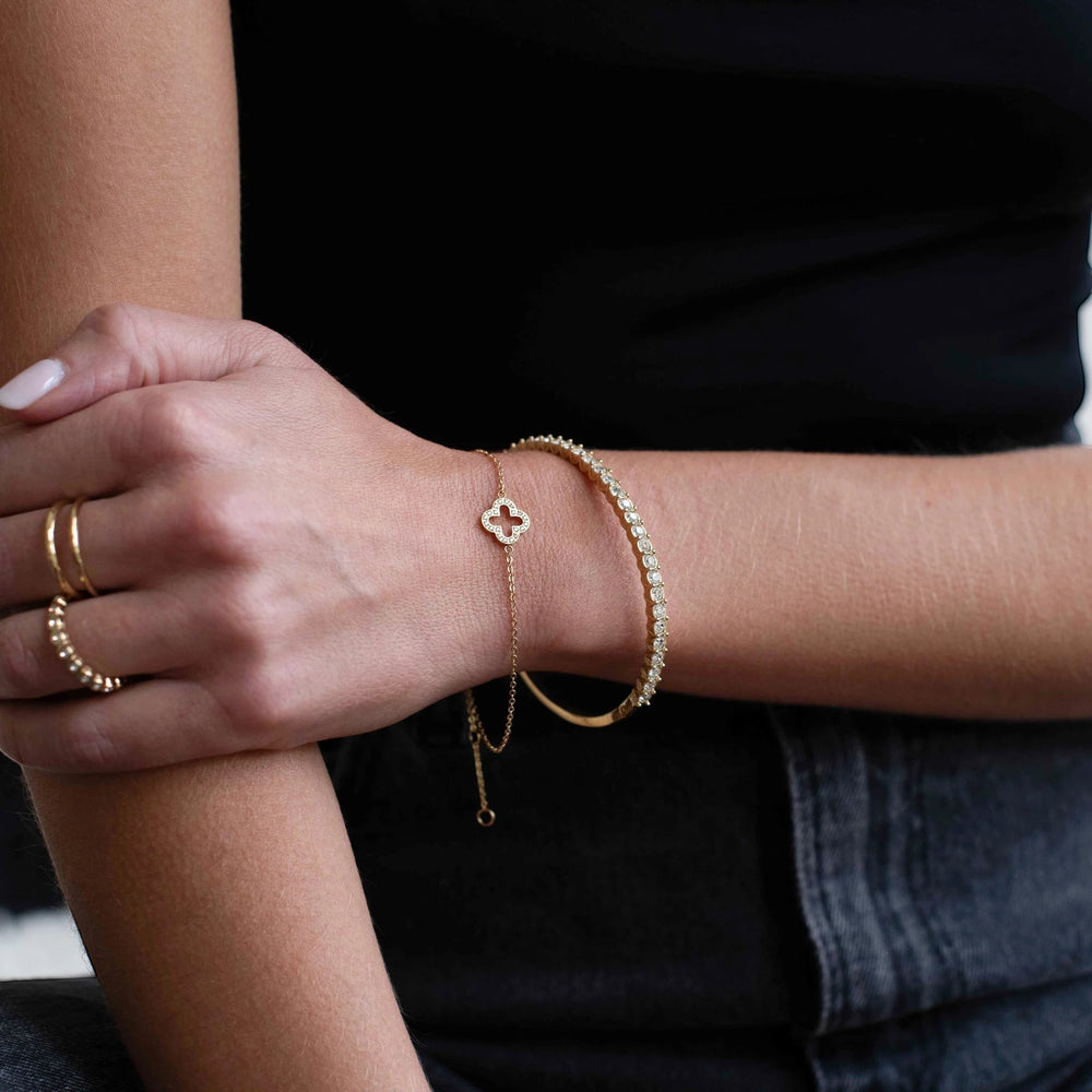 Niche Jewellery D.Louise gold pavé clover bracelet worn on a wrist with a matching tennis bracelet and gold rings.