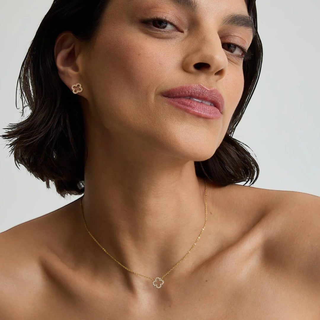 Niche Jewellery D.Louise gold pavé clover pendant necklace worn by a woman with matching clover stud earrings