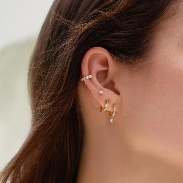 Niche Jewellery gold huggie hoop earrings featuring pavé cubic zirconia and bezel-set stones worn in an ear stack.