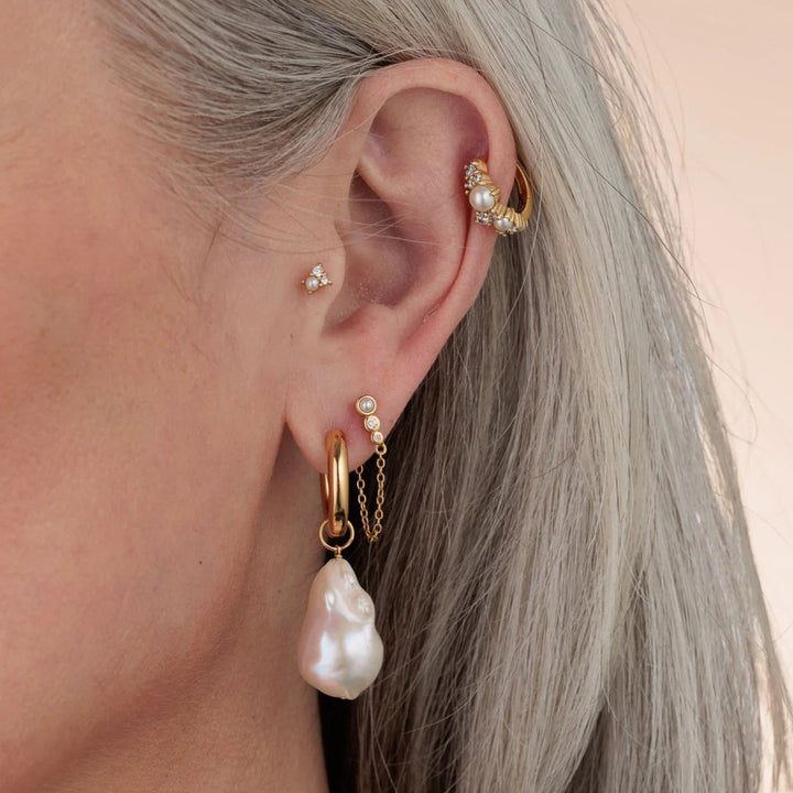 Niche Jewellery Scream Pretty Hannah Martin gold huggie earrings with lustrous pearl drops worn on a model ear
