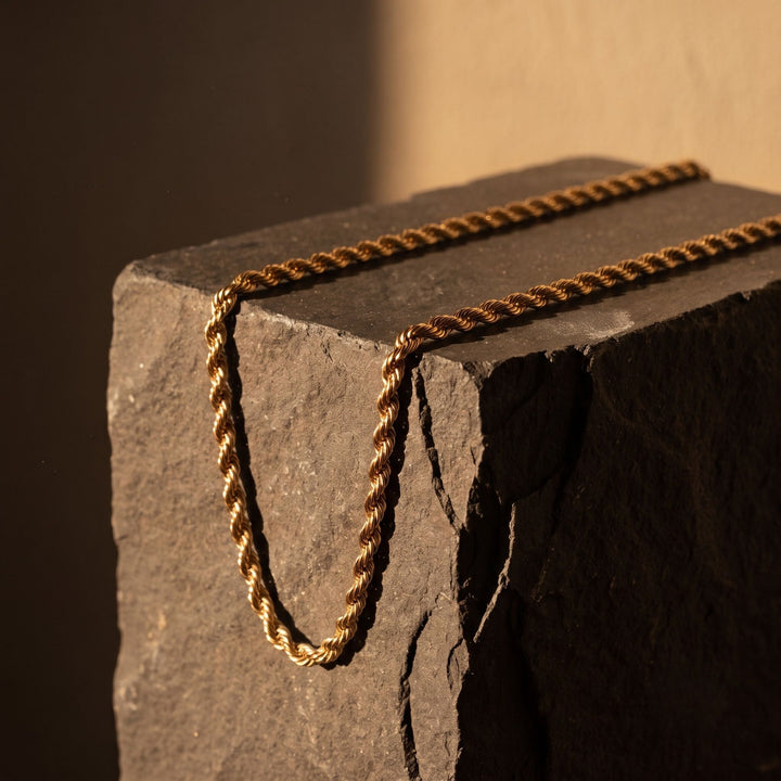 Niche Jewellery gold twisted rope chain necklace made from 316L stainless steel resting on a dark stone block