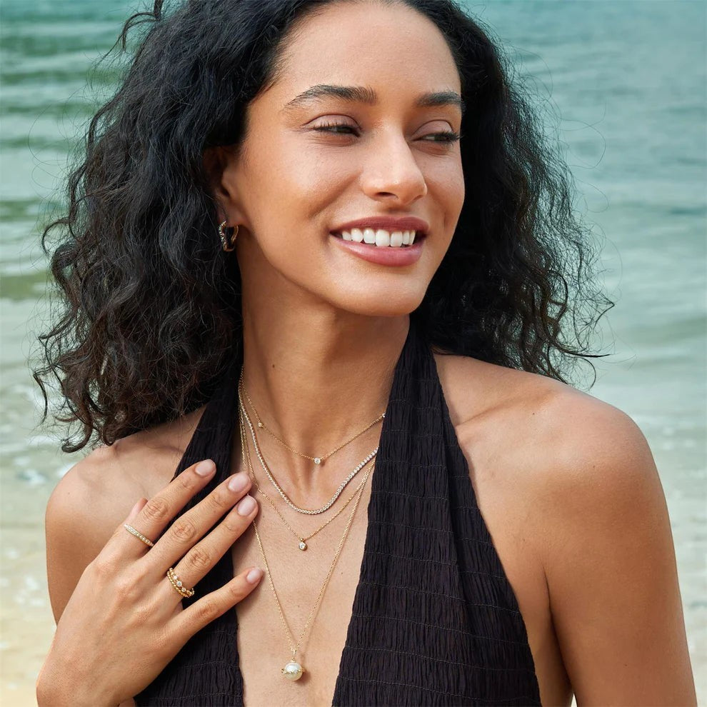 Niche Jewellery Ania Haie gold solitaire necklace with bezel-set cubic zirconia worn by a smiling woman at the beach