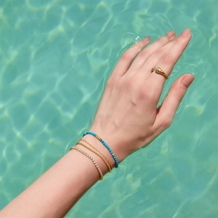 Niche Jewellery Ania Haie textured gold chain bracelet worn with beaded and crystal bracelets in pool water