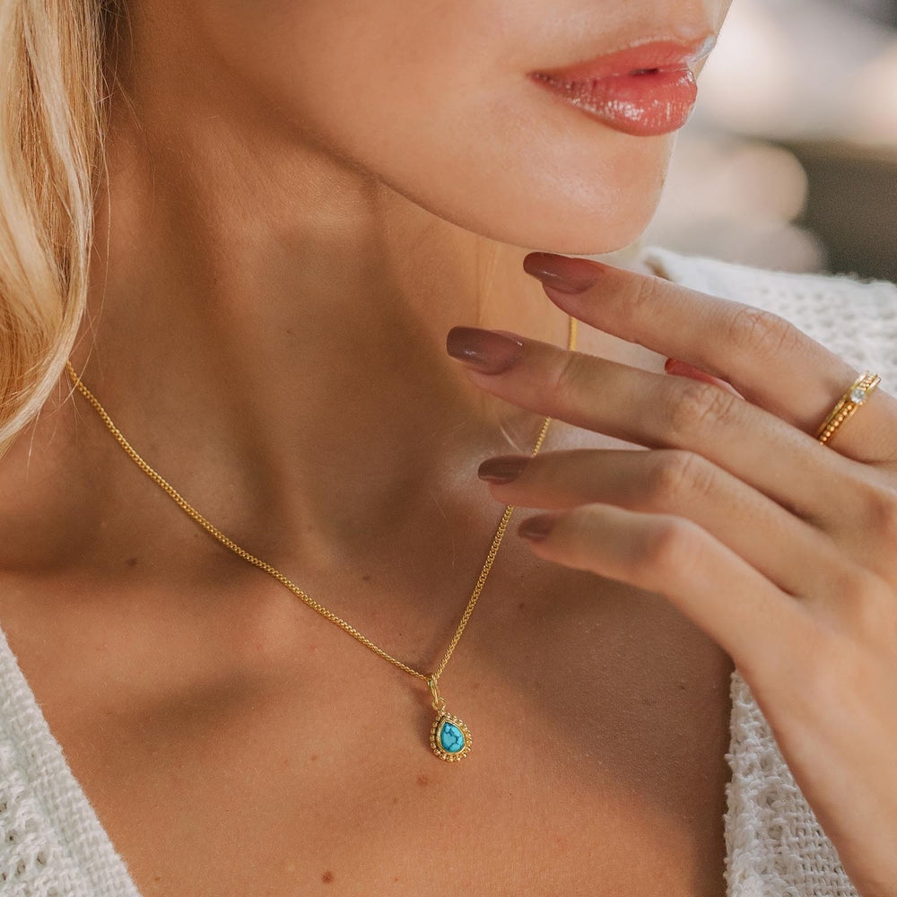 Niche Jewellery Charlotte's Web gold-plated necklace featuring a pear-shaped turquoise pendant worn by a woman.
