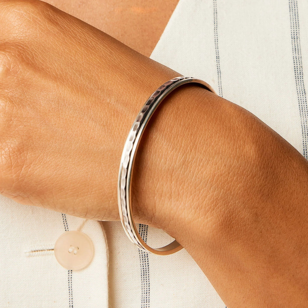 Niche Jewellery Charlotte's Web sterling silver hammered spinning stacking bangle worn on a wrist with a white striped shirt.