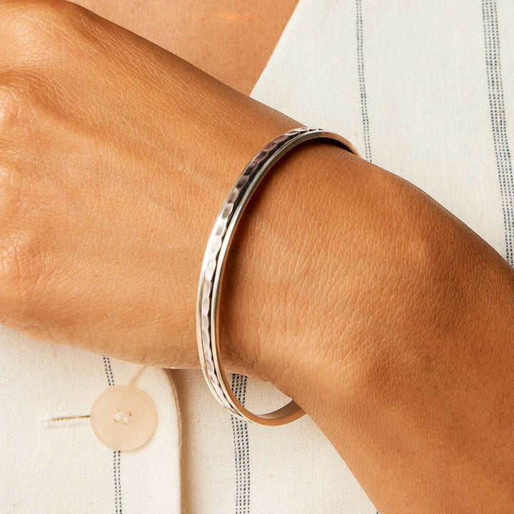Niche Jewellery Charlotte's Web sterling silver hammered spinning stacking bangle worn on a wrist with a white striped shirt.