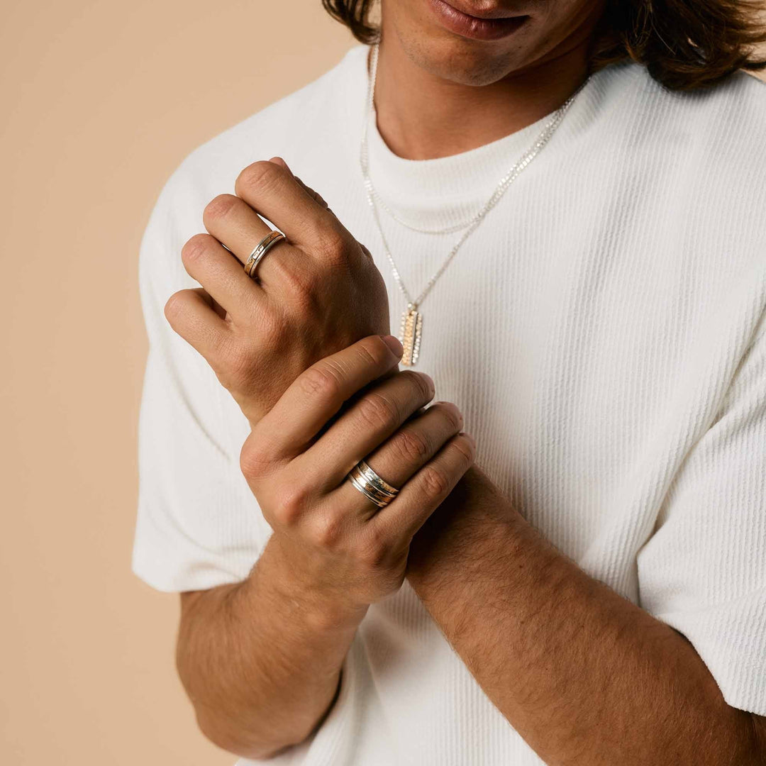 Niche Jewellery Charlotte's Web Karma Fortune unisex mixed metal spinning ring worn on a man's fingers.