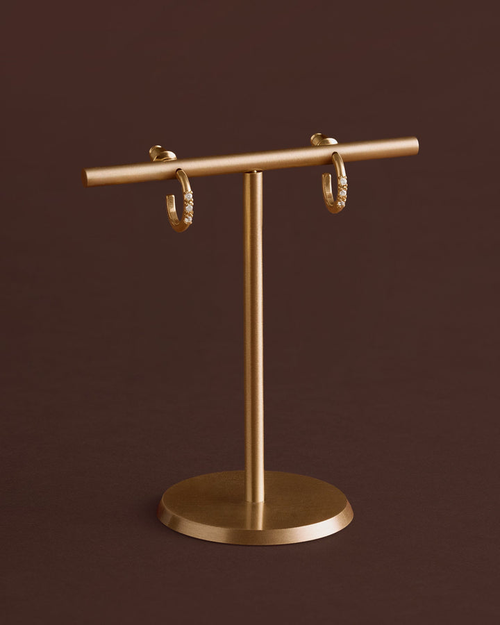 Niche Jewellery Katie Loxton Lumira waterproof gold hoop earrings with small crystal accents on a gold display stand.