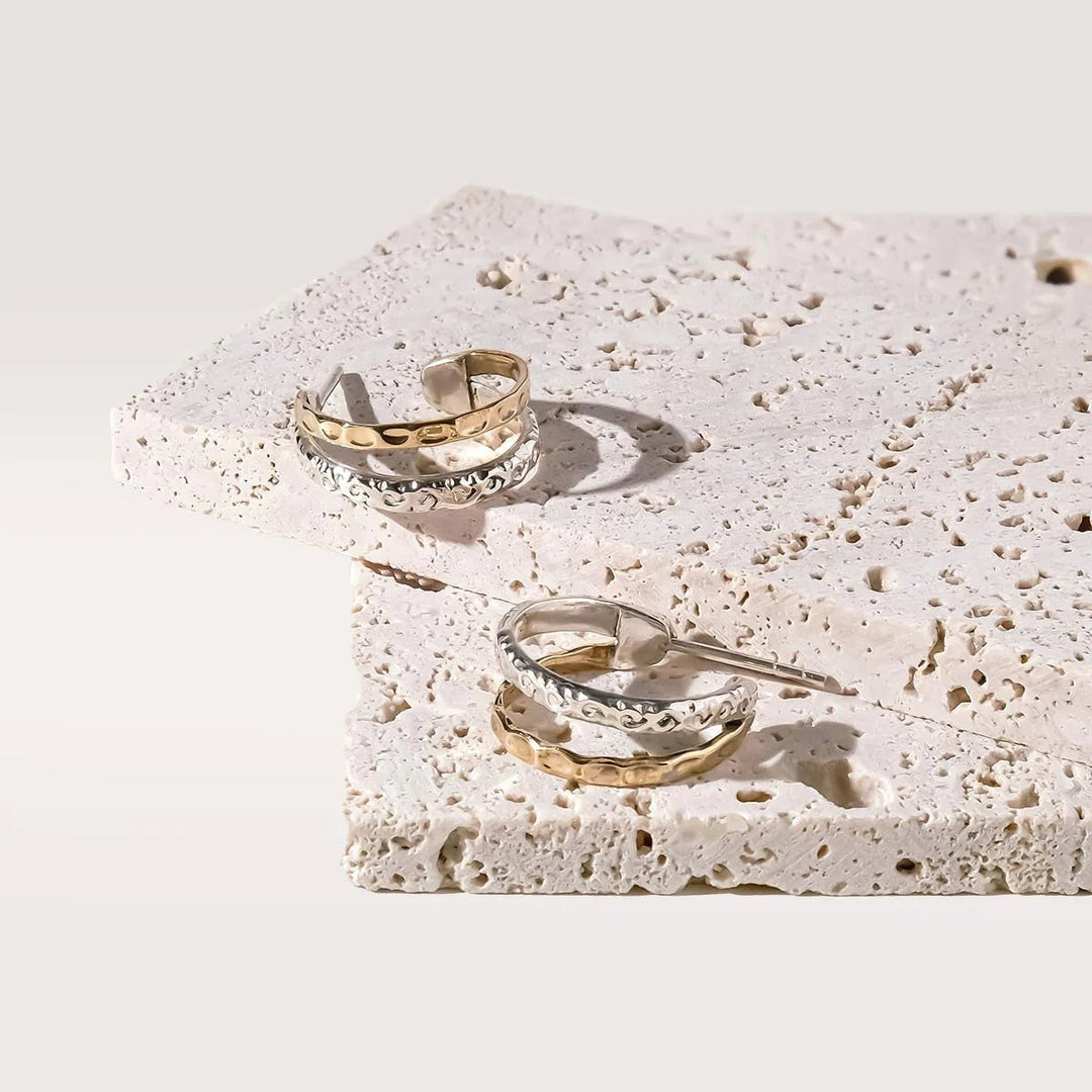 Niche Jewellery Charlotte's Web Aura Magic mixed metal double hoop earrings with silver and bronze floral motifs on stone display.